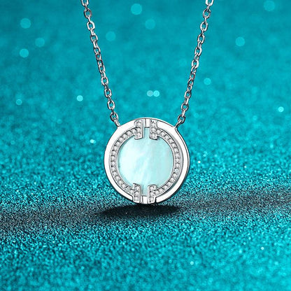 Close-up of circular moissanite necklace on a turquoise surface, emphasizing the pendant's mother-of-pearl and moissanite details.