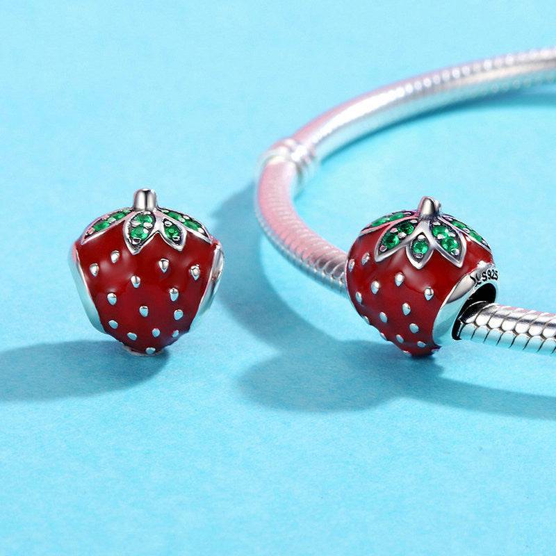 Pair of Strawberry Charms attached to a silver bracelet, showcasing their vibrant red enamel and green crystal leaves for a stylish summer accessory.