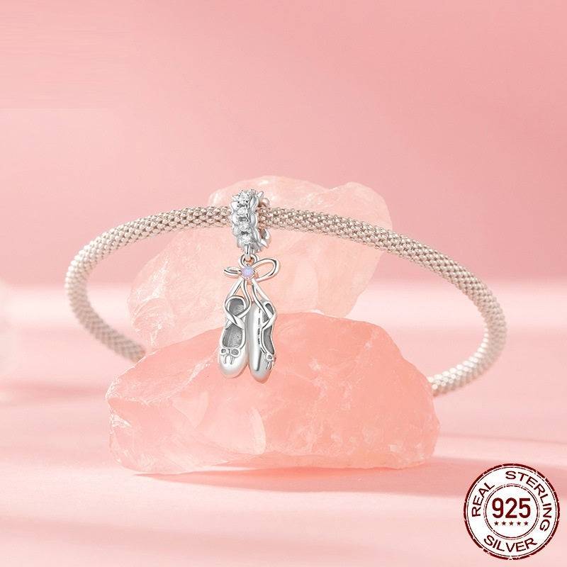 Silver Ballet Shoes Charm on a bracelet displayed on pink crystal stones. Features zircon accents and a bow design for elegance.